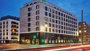 A modern hotel with multiple floors, a prominent 'Léger Express' sign, and a well-lit facade. - LÉGÈRE EXPRESS Hotel Leipzig - Apartment with kitchenette & breakfast optional (Leipzig)