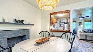 A dining area with a round table, chairs, a wooden bowl, a fireplace, and a kitchen visible through an open doorway. - Cute'N Chic 4b/2b Entire House Downtown Clayton GA (Clayton)