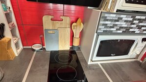 Una cocina con tope de inducción negro, un microondas, tablas de cortar de madera y un soporte de cucharas de madera.