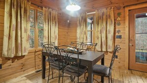 Een kamer met houten lambrisering, een eettafel met stoelen, een houten deur en ramen met gordijnen.
