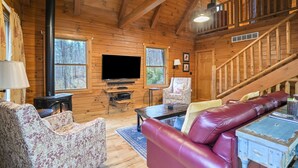 Een gezellig chaletinterieur met houten inrichting, een open haard, een televisie, een bank en een trap.