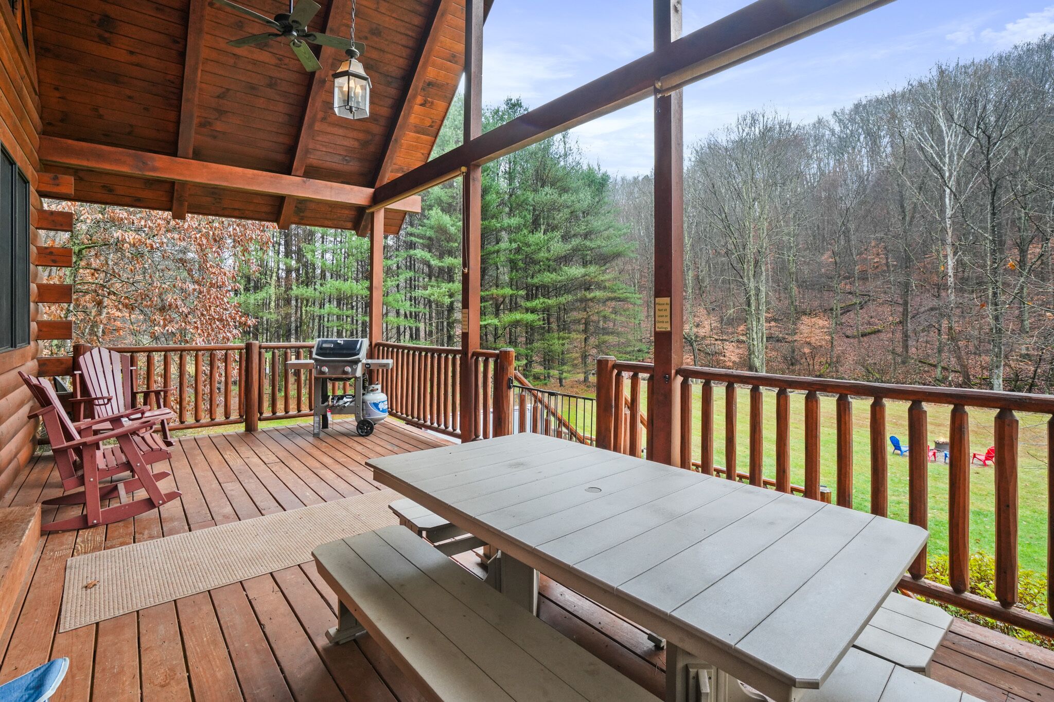 A wooden deck with a picnic table and chairs, a grill, and a view of a forested area.