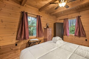 Une chambre à coucher dans une cabane en bois, avec un lit, une commode, une table de chevet et un ventilateur de plafond.