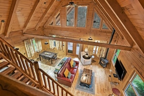 Une cabine spacieuse avec un plafond haut, des poutres en bois, une cheminée, un coin salon confortable et de grandes fenêtres.