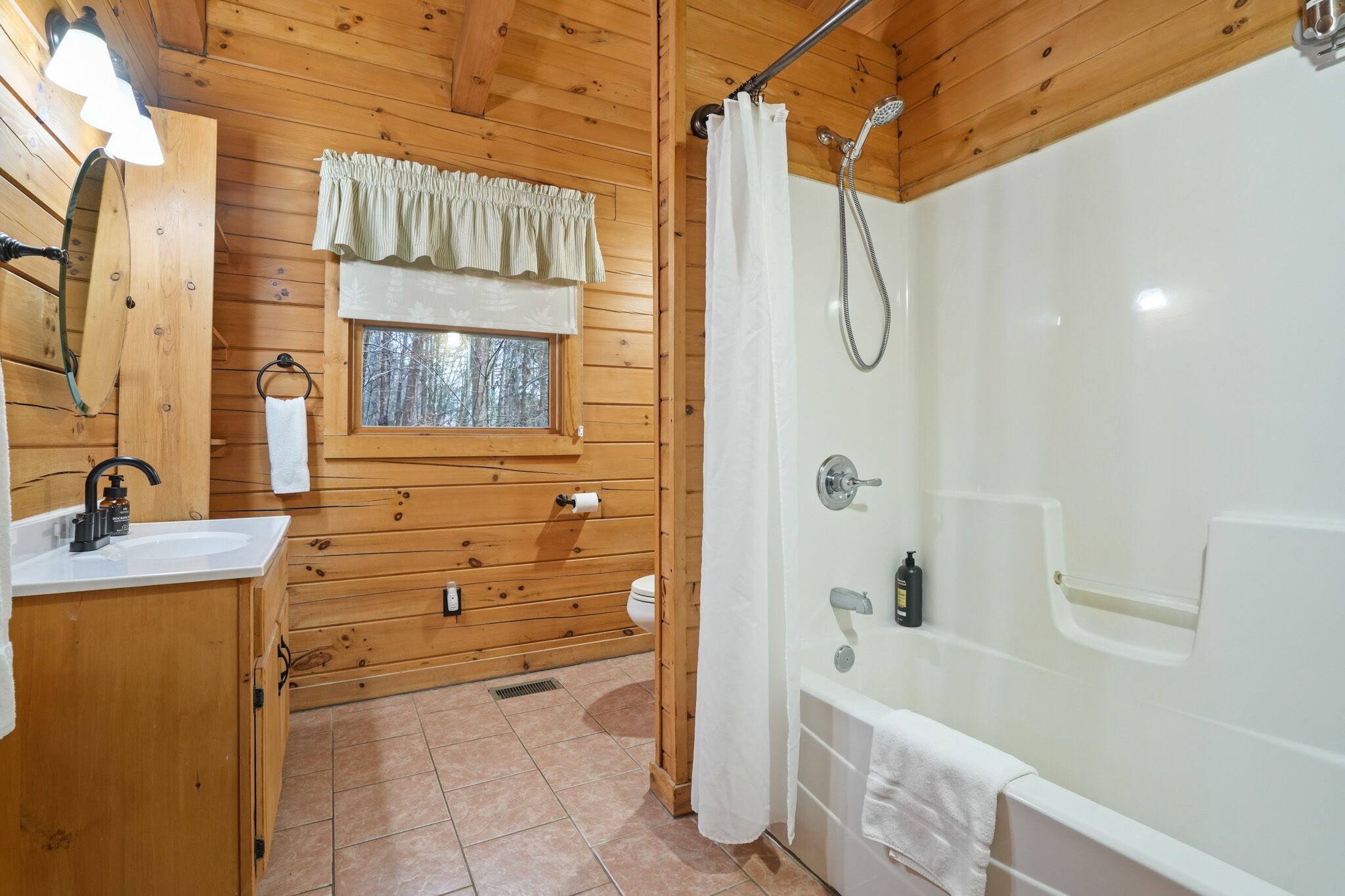 A wooden cabin bathroom with a sink, toilet, window, and a walk-in shower.