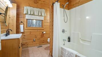 A wooden cabin bathroom with a sink, toilet, window, and a walk-in shower.
