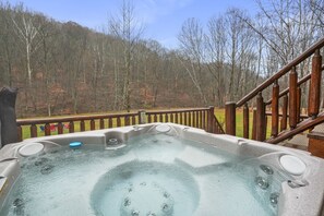 A hot tub with a wooden deck and railing, surrounded by a forested hillside. - Shadyside Cabin | Hocking Hills, Hot Tub, Firepit (Laurelville)
