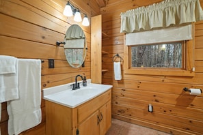 A wooden cabin bathroom with a sink, mirror, towel rack, and window. - Shadyside Cabin | Hocking Hills, Hot Tub, Firepit (Laurelville)