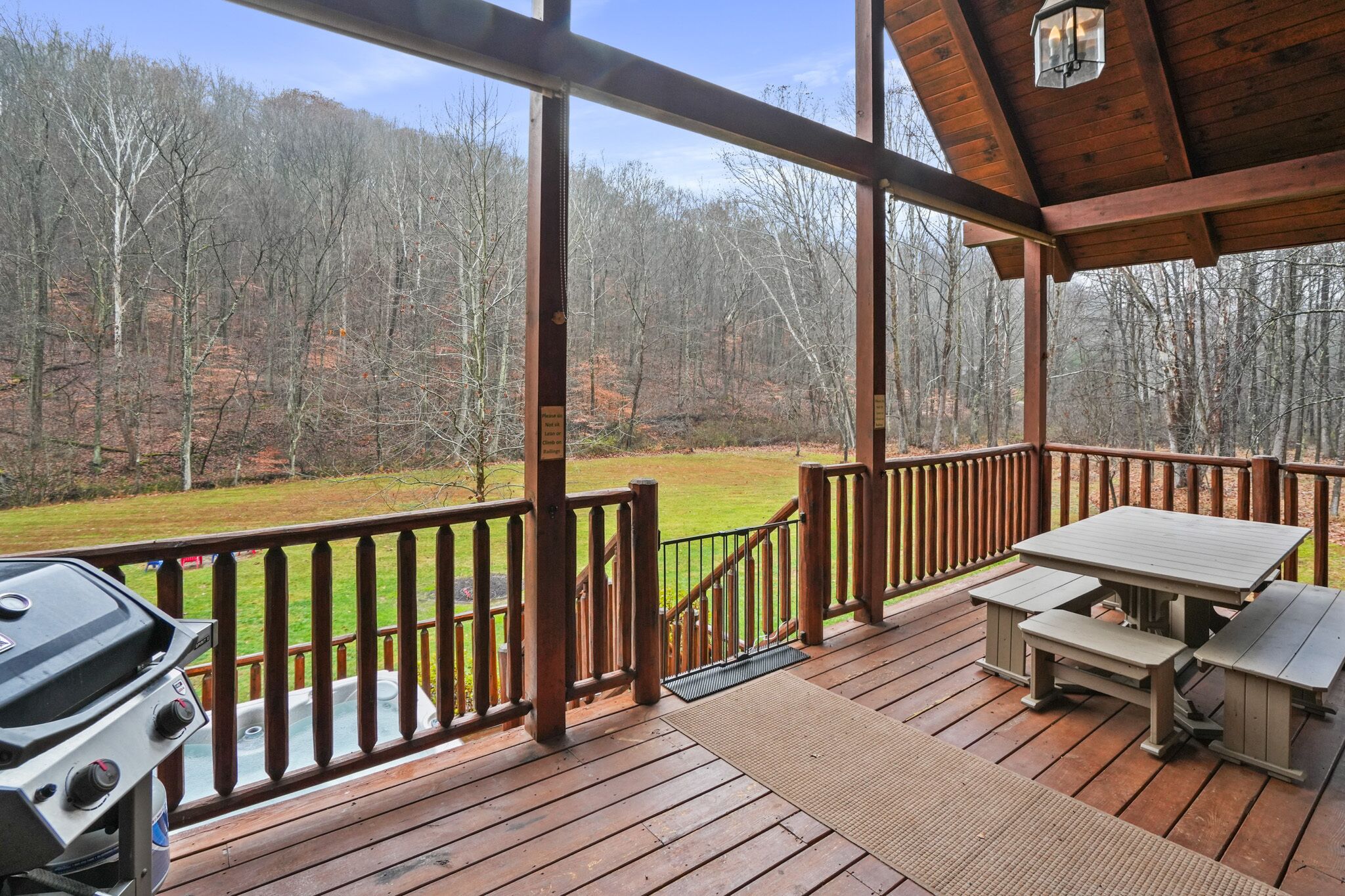 A wooden deck with a barbecue grill and picnic table, overlooking a forested area.