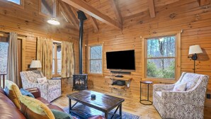 Een gezellig interieur van een chalet met houten wanden, een open haard, een televisie en comfortabele zitplaatsen.