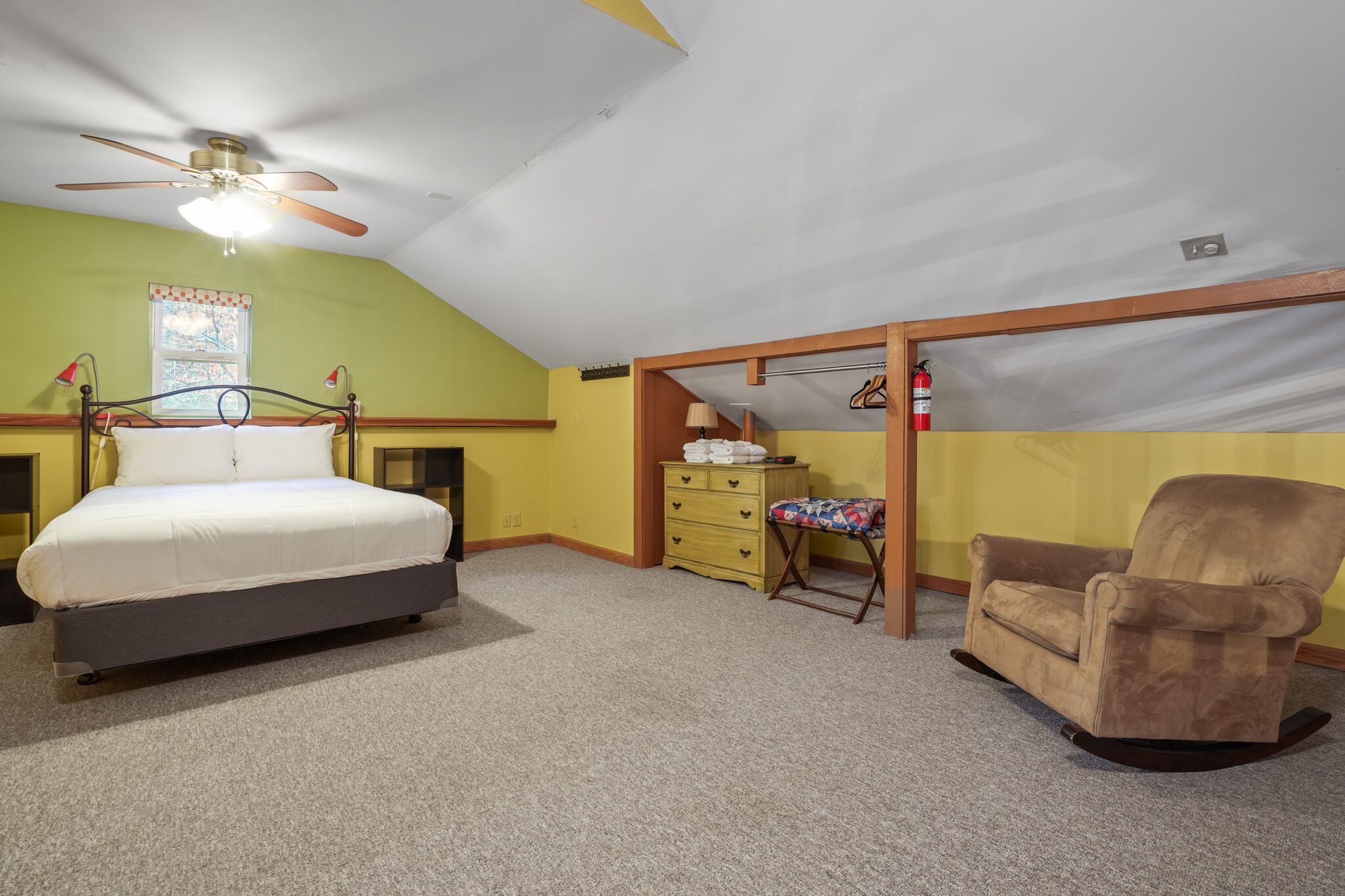 A bedroom with a bed, a rocking chair, a dresser, and a ceiling fan.