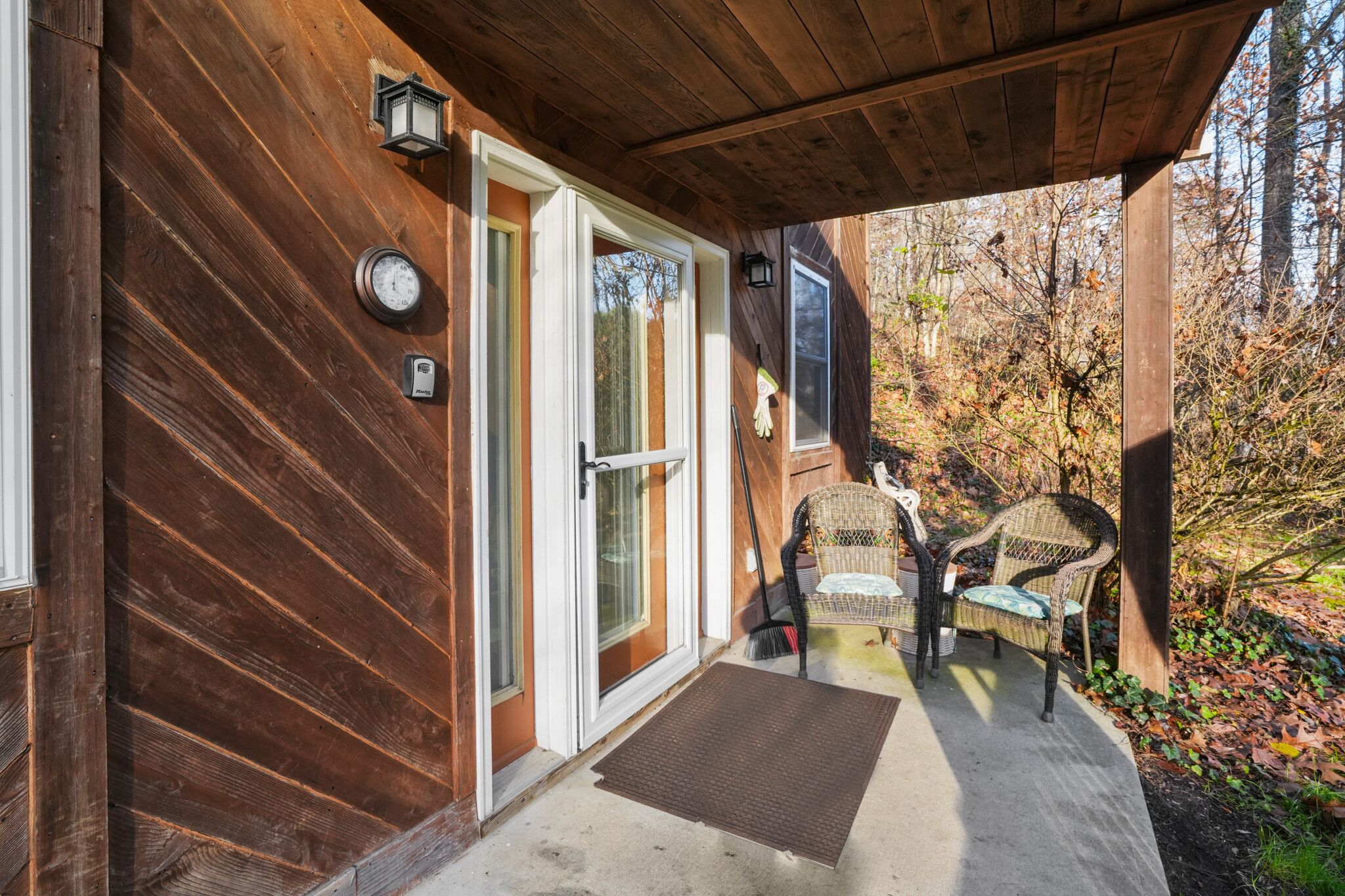 Une façade en bois avec une porte-fenêtre coulissante, un petit porche avec des fauteuils en osier et une terrasse en bois.