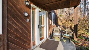 Une façade en bois avec une porte-fenêtre coulissante, un petit porche avec des fauteuils en osier et une terrasse en bois.