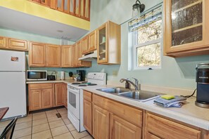 Una cocina con armarios de madera, un refrigerador blanco, un microondas, una estufa, un fregadero y una cafetera.