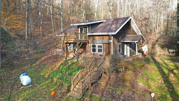 Une maison en bois à deux étages, dotée d’un balcon et entourée d’une forêt.