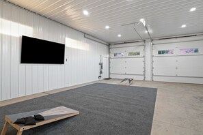 A spacious indoor area with a large flat-screen TV mounted on the wall, a grey carpeted floor, and a wooden bench with cushions.
