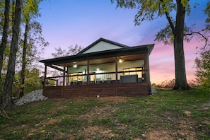 A modern house with a large porch, surrounded by trees and a clear sky.