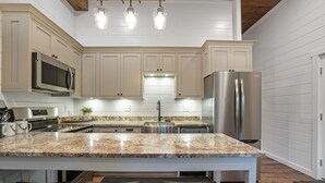 A modern kitchen with white cabinets, stainless steel appliances, a granite countertop, and pendant lighting.