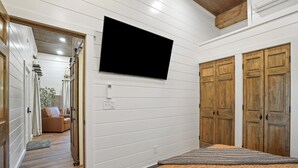 A bedroom with a bed, a television mounted on the wall, wooden doors, and a hallway leading to a living area.