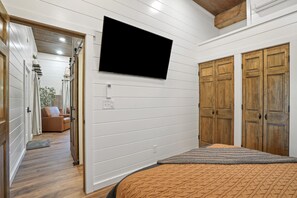 A bedroom with a bed, a television mounted on the wall, wooden doors, and a hallway leading to a living area. - The Ivory Buck | Hocking Hills, Unique, Fun (Sugar Grove)
