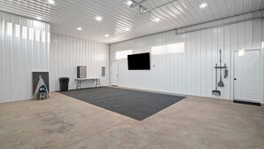A spacious indoor area with a large carpeted floor, white walls, a mounted TV, and a door with a broom hanging on it.