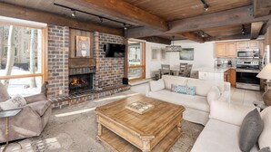 A cozy living room with a fireplace, a sofa, a coffee table, and a kitchen area with modern appliances. - Top of the Village~Ski-in/out~HT~Pool~Grill~Parking (Snowmass Village)