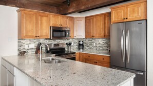A kitchen with wooden cabinets, stainless steel appliances, a granite countertop, and a tiled backsplash. - Top of the Village~Ski-in/out~HT~Pool~Grill~Parking (Snowmass Village)