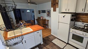 A compact kitchen with white cabinets, a wooden countertop, a stove, and a refrigerator. - Grandma's Cozy 2-bedroom retreat (Muskegon)