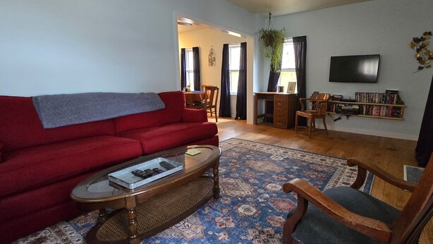 A living room with a red sofa, a coffee table with remotes, a wooden chair, a bookshelf, and a TV on the wall. - Grandma's Cozy 2-bedroom retreat (Muskegon)