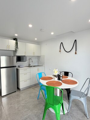 A modern kitchen with white cabinets, stainless steel appliances, and a dining area with a round table and colorful chairs. - Villa Margarita Luxury M1,a 5 min del aeropuerto SJU, playas y restaurantes. (carolina)