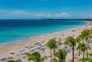 A beach with rows of sun loungers and umbrellas, palm trees, and a clear view of the ocean. - Villa Margarita Luxury M1,a 5 min del aeropuerto SJU, playas y restaurantes. (carolina)