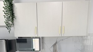 Ett kök med vita skåp, ett kylskåp i rostfritt stål, en mikrovågsugn, en diskho och en väggbeklädnad av marmor bakom diskbänken.