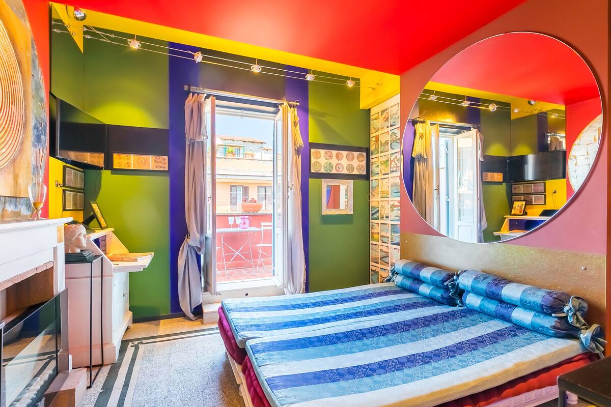 Una habitación luminosa y colorida con una cama, un espejo y una ventana con cortinas.