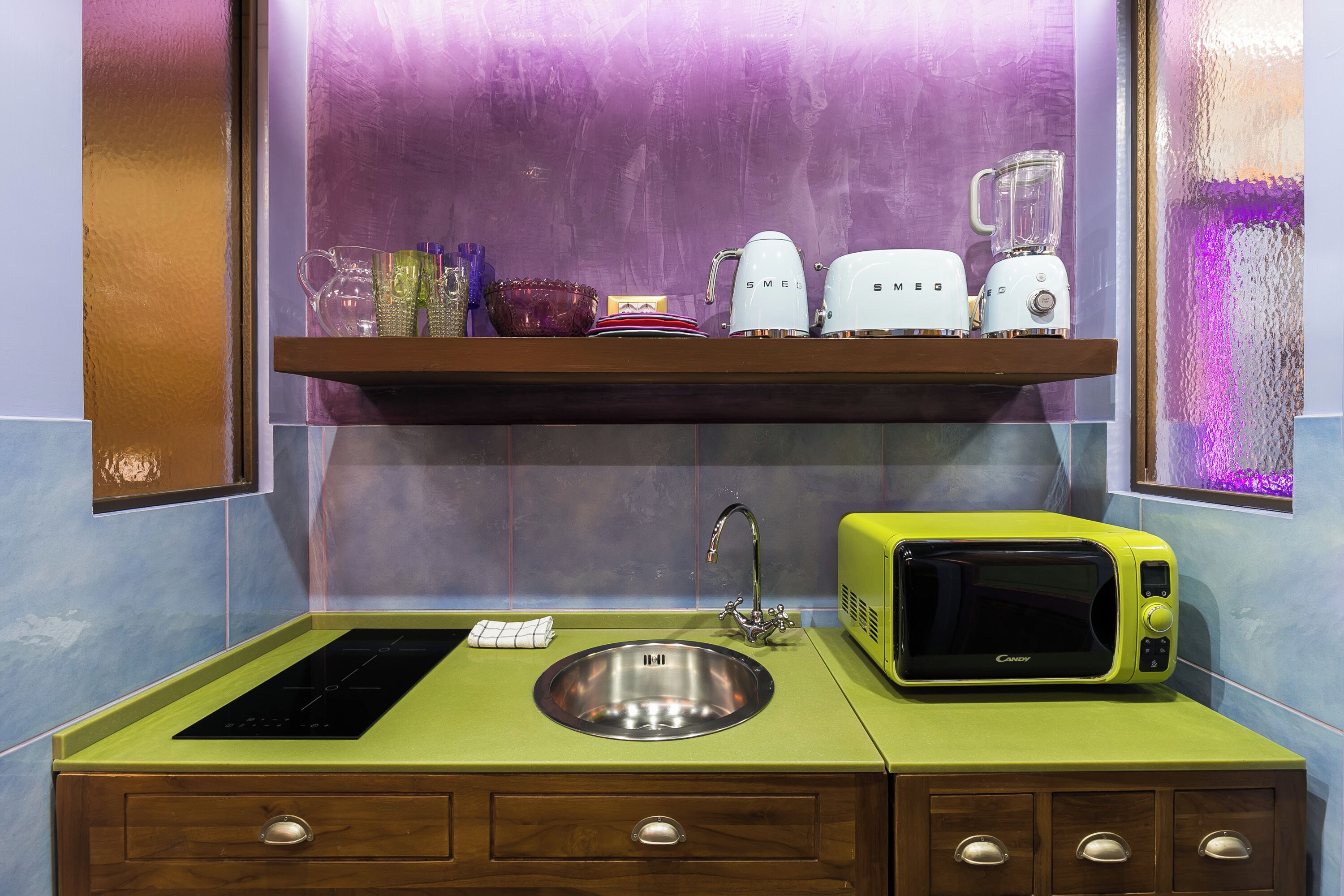 A kitchen with a green countertop, stainless steel sink, and a microwave.