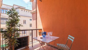 Un balcon avec une table, des chaises, un pot de fleurs et un téléviseur.