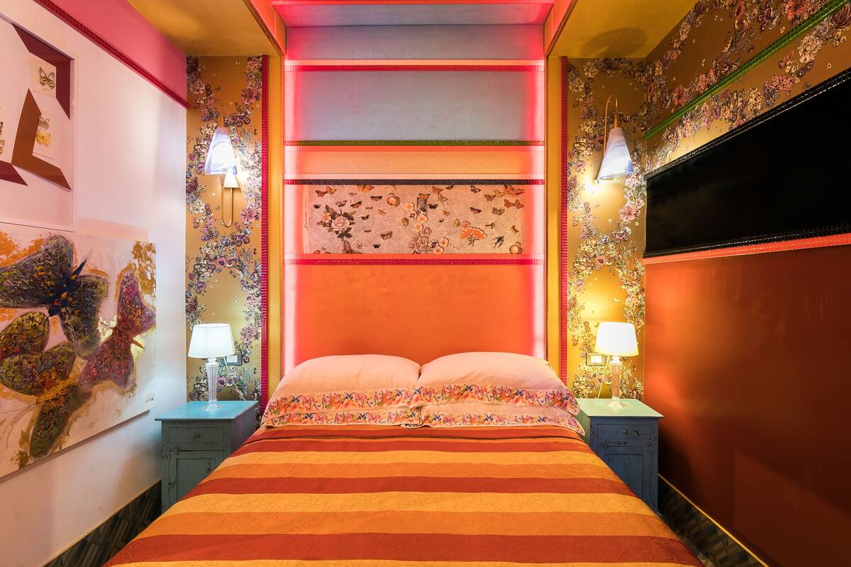 Una cama con ropa de cama a rayas, un cabecero floral y dos lámparas de noche.