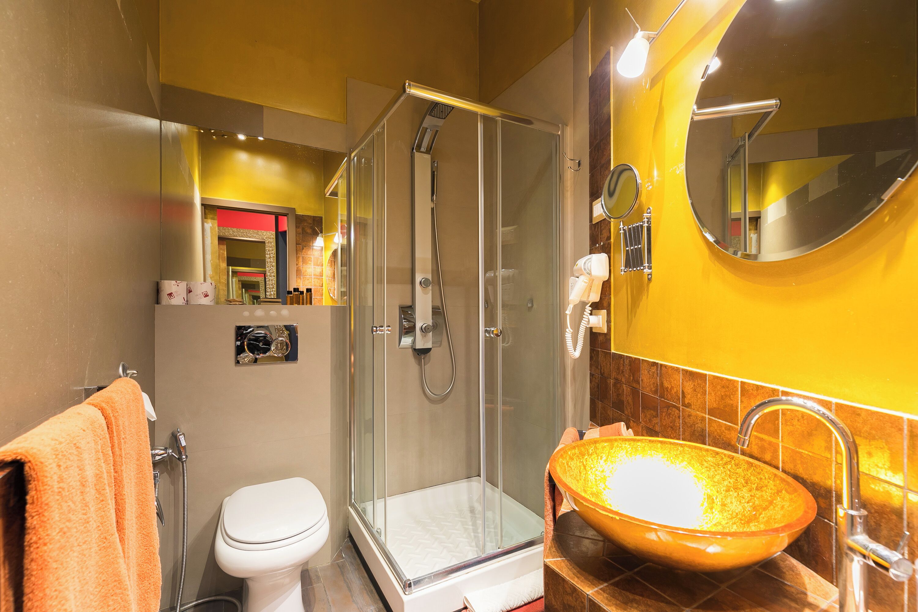 A bathroom with a glass-enclosed shower, a white toilet, and a large oval sink with a gold finish.