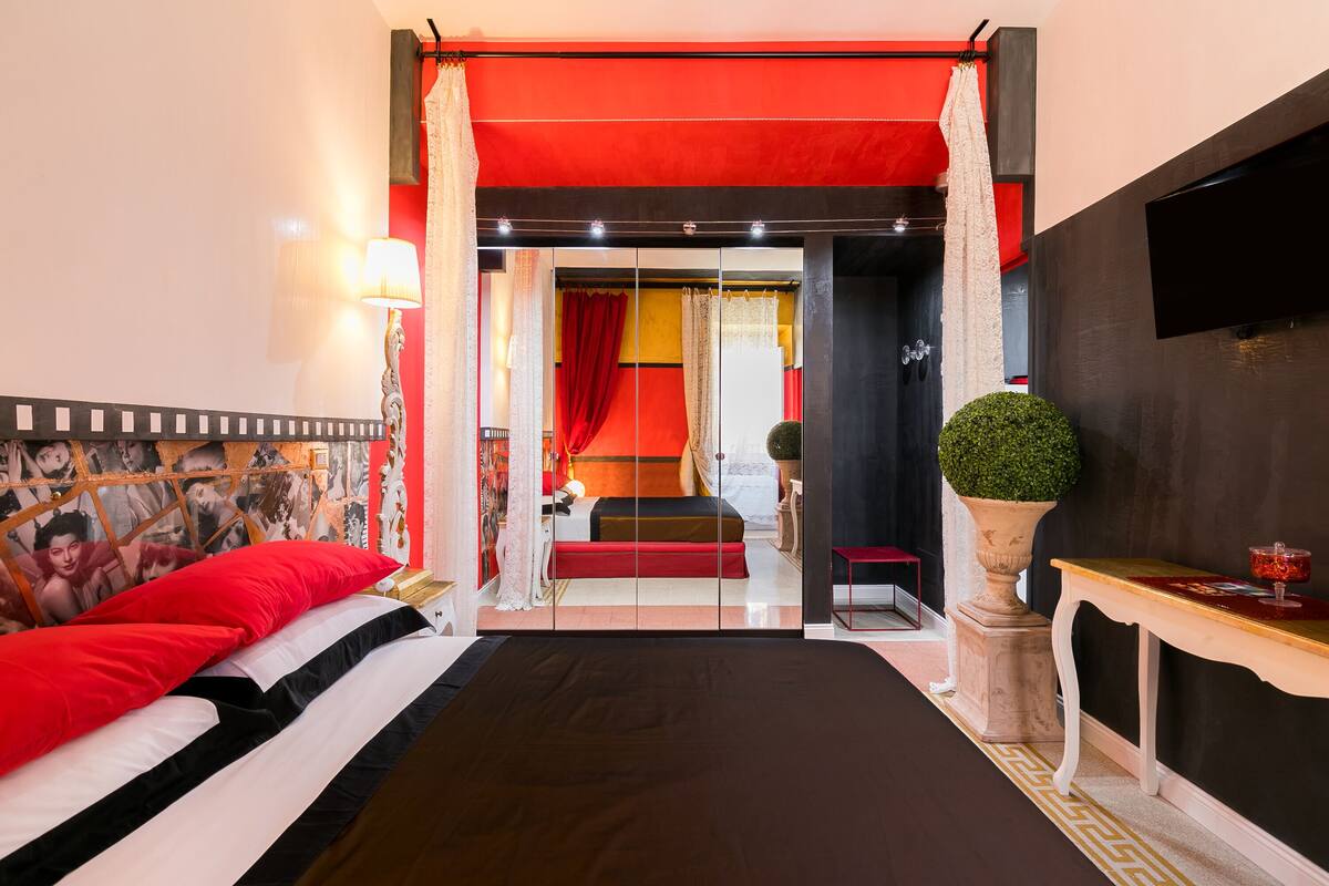 Un dormitorio con cama, mesita de noche, lámpara, televisor y un amplio ventanal.