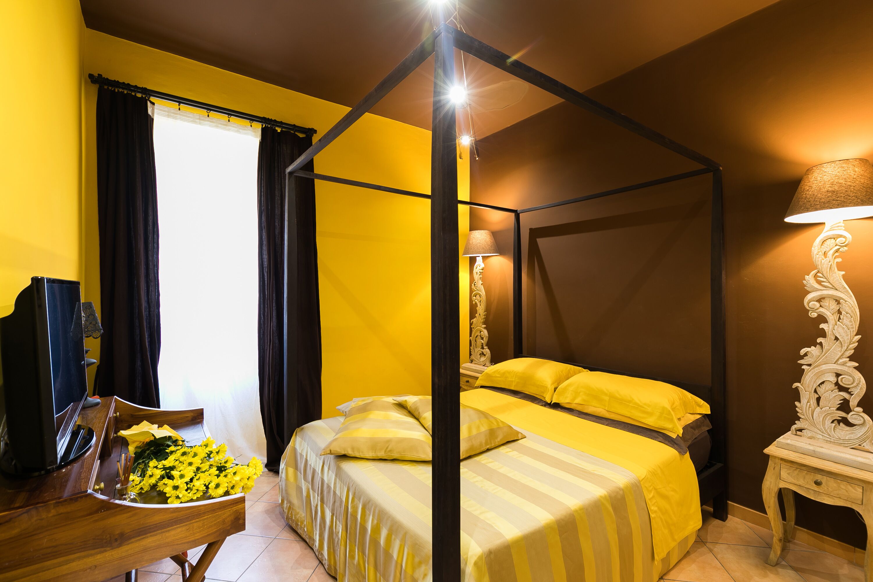 A room with a four-poster bed, a wooden desk with a lamp, and a television.