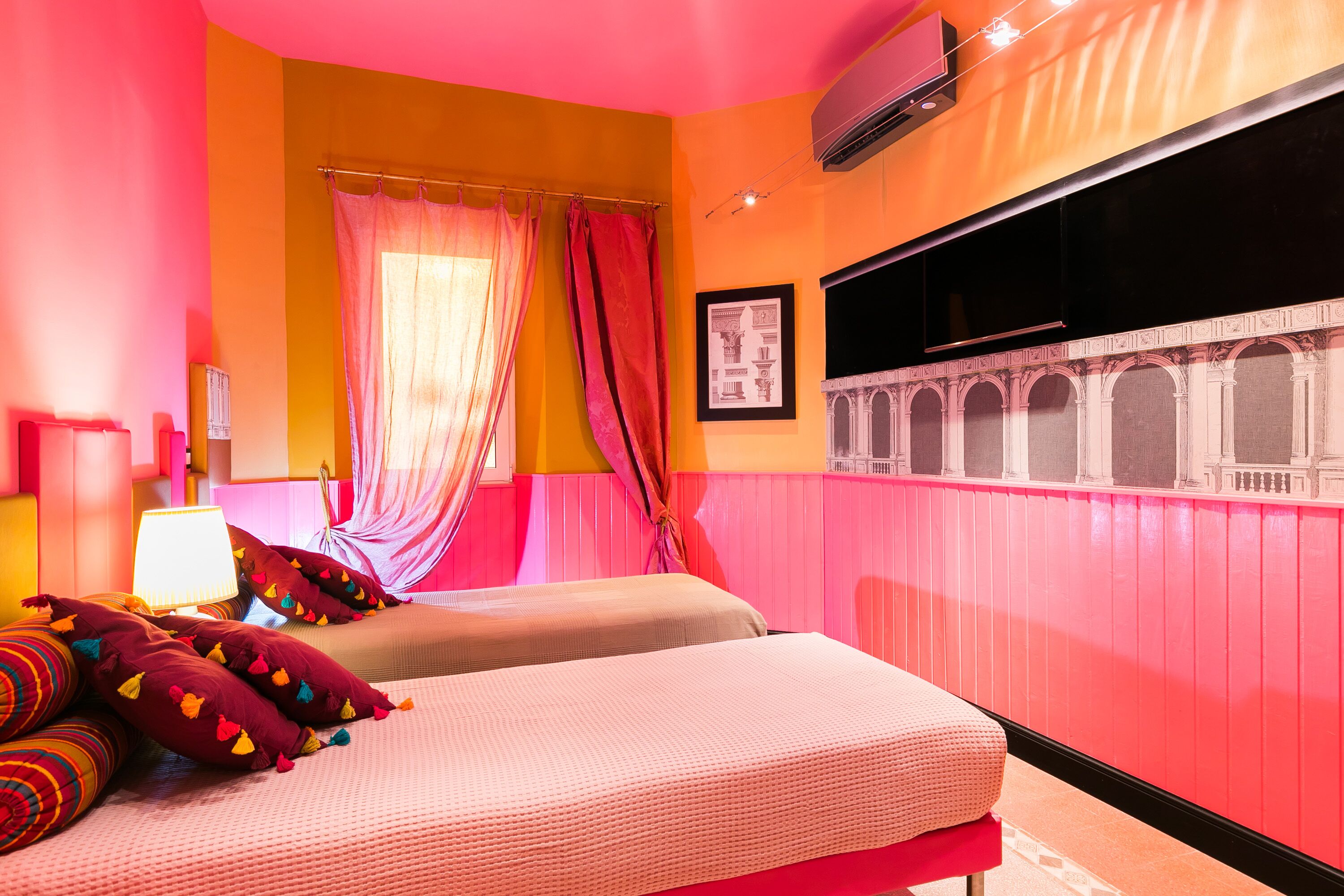 A room with two beds, a window with a view of a building, and a wall-mounted air conditioner.