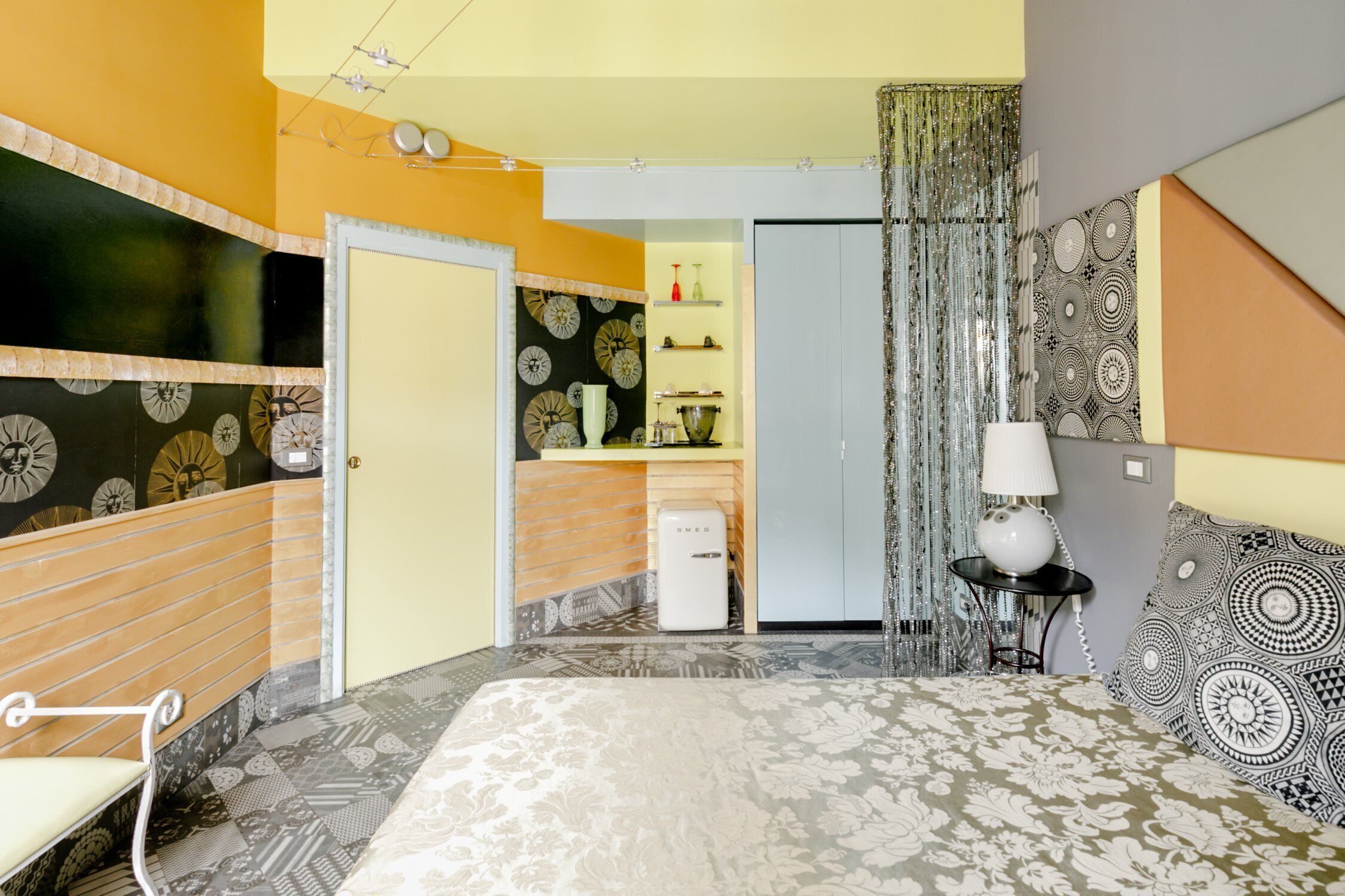 Un dormitorio con cama, mesita de noche, lámpara, sillón, armario y una pequeña kitchenette.