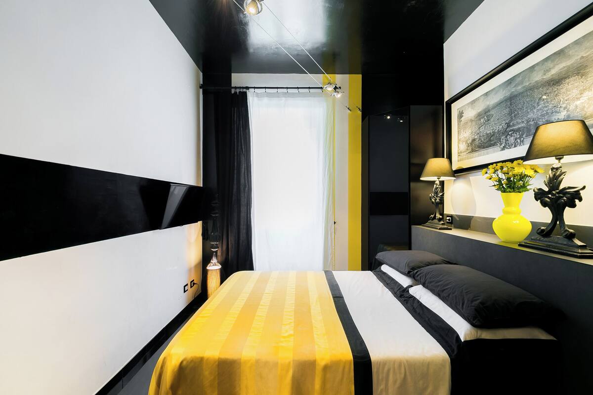 Una habitación de hotel moderna con una cama, lámparas de noche, un cuadro y un florero con flores.