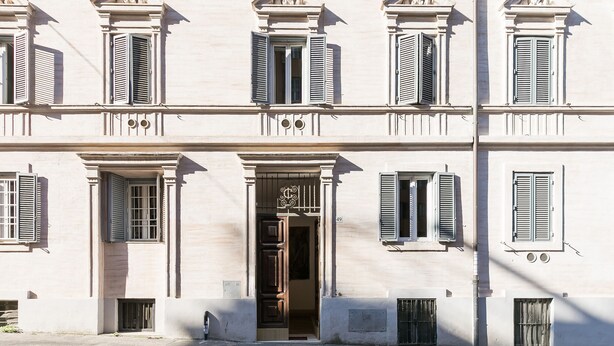Un bâtiment doté de nombreuses fenêtres, dont certaines sont équipées de volets, et d’une entrée centrale avec une porte.
