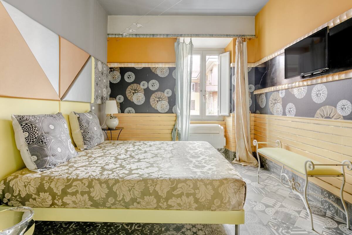 Una habitación de hotel con cama, un banco, un televisor y una ventana con cortinas.