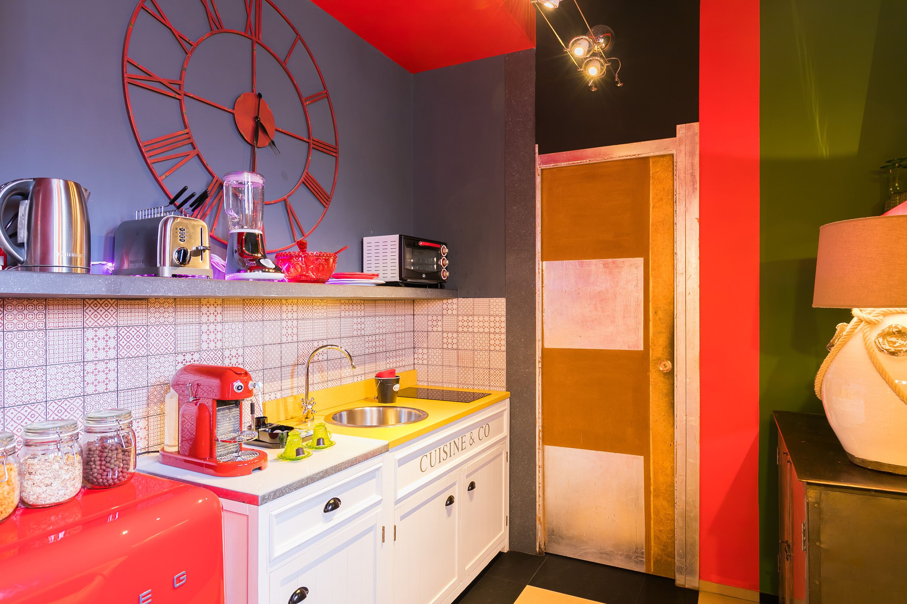 A kitchen with a red and white color scheme, a large wall clock, and various appliances.