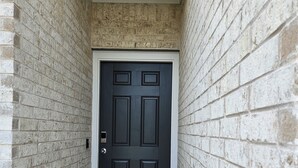A narrow brick corridor leading to a dark door with a doormat reading "Welcome". - Stylish 4BR Home, perfect for families, professionals, business & group stays. (Sherman)