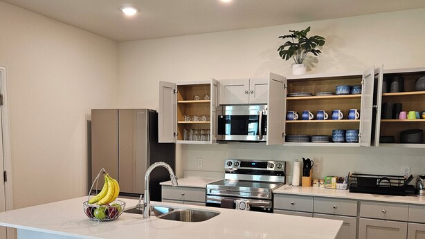 A modern kitchen with a central island, bar stools, stainless steel appliances, and open shelving with dishes. - Stylish 4BR Home, perfect for families, professionals, business & group stays. (Sherman)