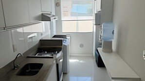 Une cuisine étroite et blanche, équipée d’un four encastré, d’un évier et d’un petit réfrigérateur.