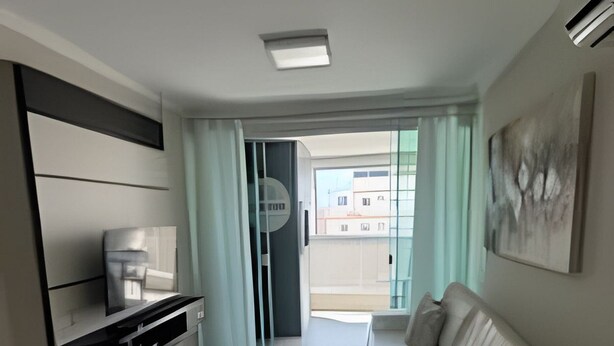 Un salon moderne avec un canapé, une table basse et un téléviseur. Une porte-fenêtre coulissante donne accès à un balcon.