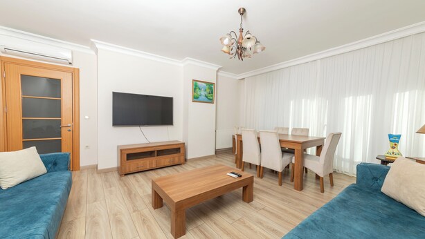 A living room with a wooden coffee table, blue sofas, a TV, and a dining area with chairs and a table. - FAMILY HOME (İstanbul)